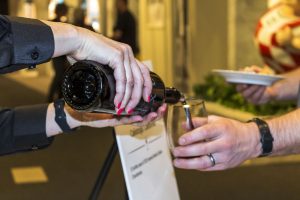 A server pours red wine from a bottle into a stemless glass held by another person