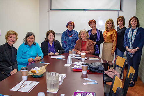 A group of women sit and stand around a table with María Tomás-Keegan
