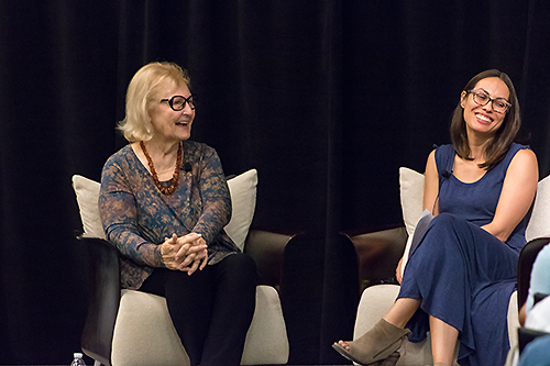 Pauline Boss and Kathy Ritchie sit in armchairs on a stage