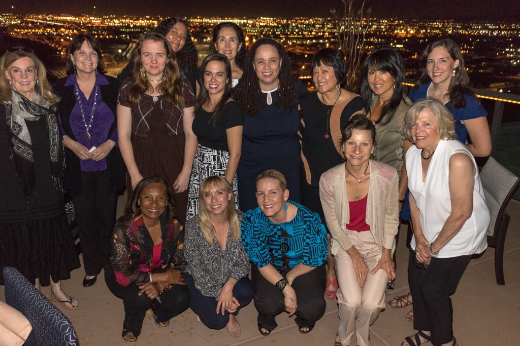 A group of women pose on a rooftop patio in front of the city lights